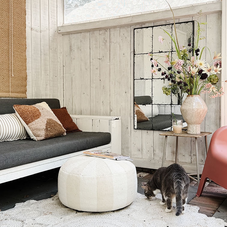 Soggiorno accogliente con parete in legno bianco, divano grigio, pouf bianco e decorazioni floreali