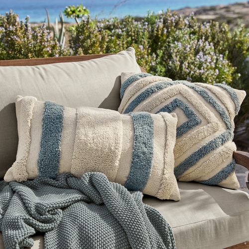 Cuscini decorativi beige e blu in materiale morbido su divano grigio all'aperto, tessuti da giardino