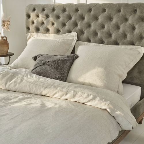 Biancheria da letto beige in lino su letto con testiera grigia capitonné, tessuto naturale per camera