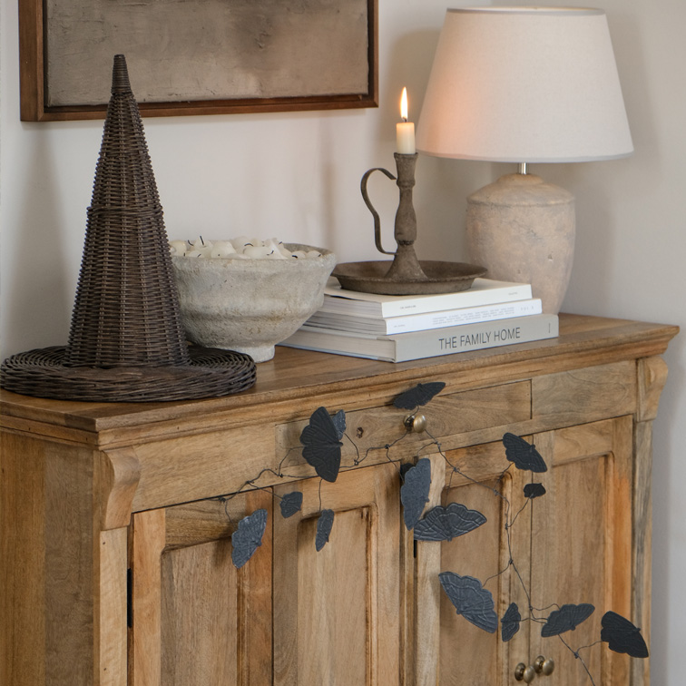 Credenza in legno con ghirlanda di foglie nere, lampada e portacandele su libri in soggiorno