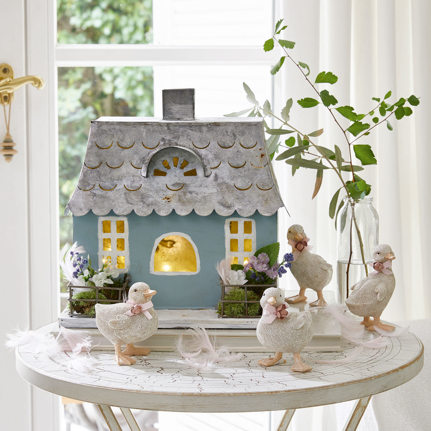 Casetta decorativa Nesrine Casetta decorativa in metallo blu con quattro paperelle bianche e fiori su tavolo bianco rotondo
