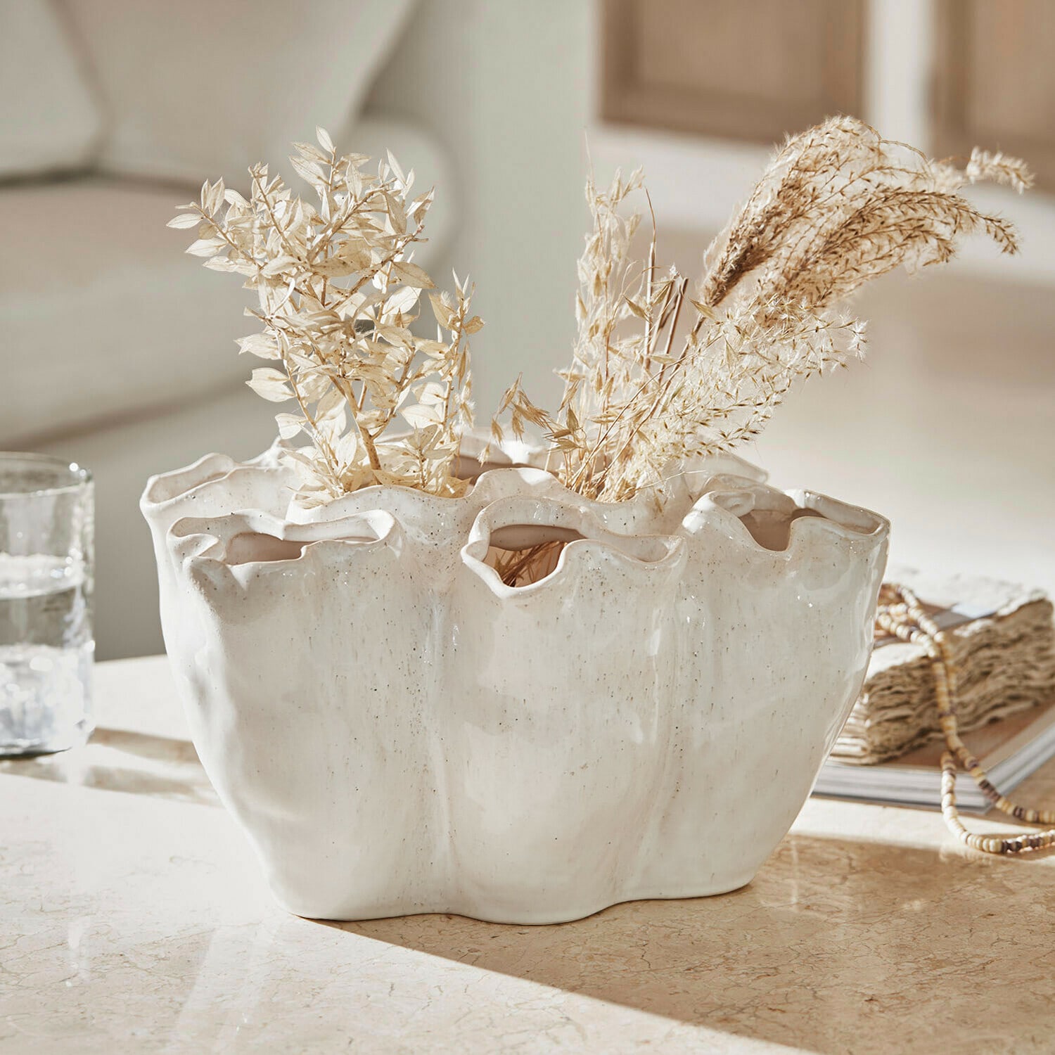 Vaso Rovinia Vaso in ceramica bianca con bordo ondulato e piante secche su tavolo decorativo