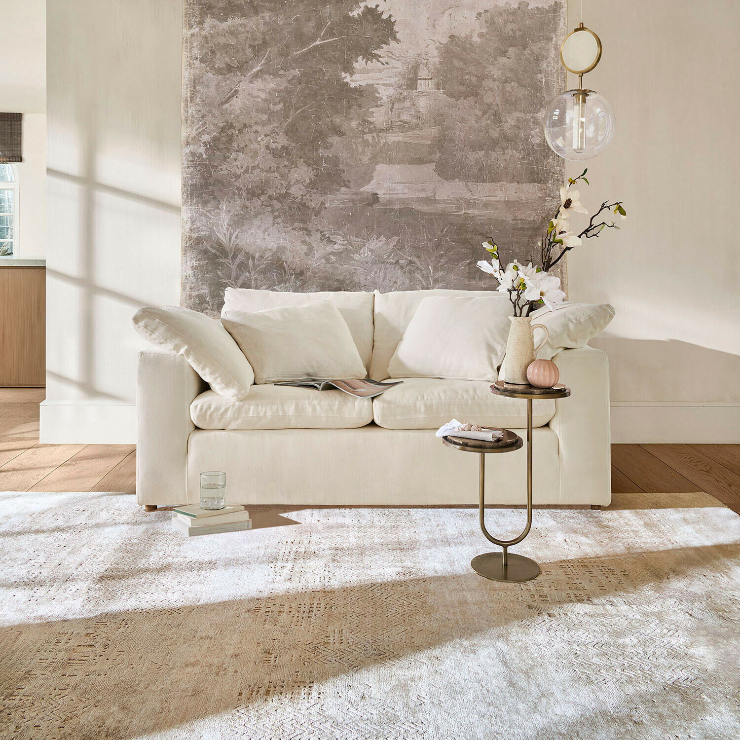 Divano Everholt Divano beige con cuscini morbidi davanti a parete con murale decorativo e tavolino con fiori