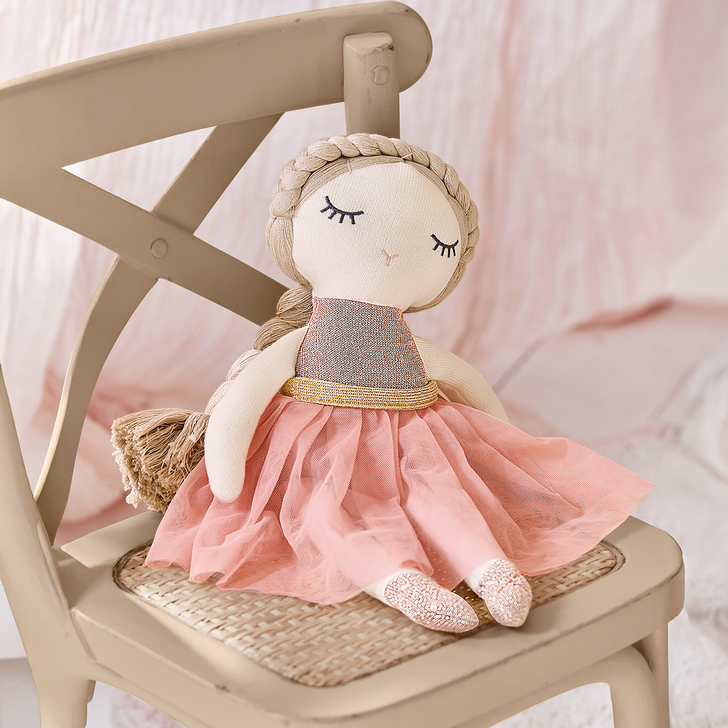 Bambola di stoffa con vestito rosa e cintura dorata seduta su sedia beige, giocattolo per bambini