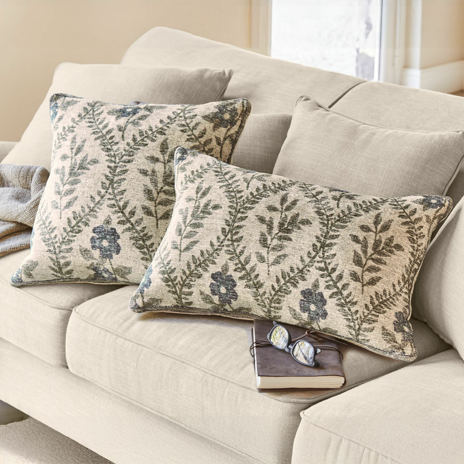 Coppia di copricuscini Vellouris Divano beige con due cuscini decorativi in tessuto con motivo di foglie verdi e fiori