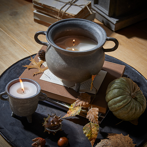 Candela in contenitore di ceramica grigia con manici su tavolo in legno con decorazioni autunnali