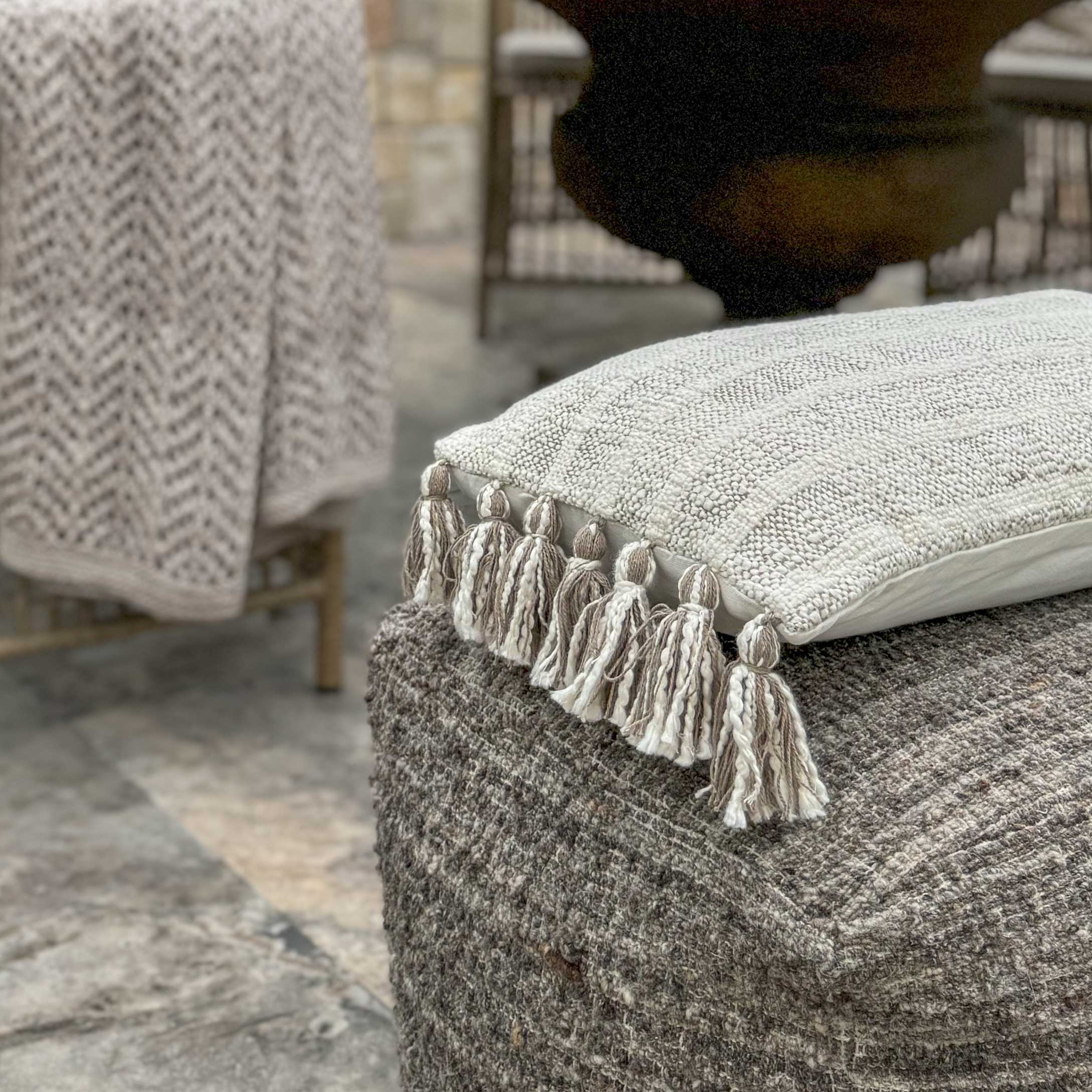 Cuscino decorativo beige con nappine su pouf grigio in lana stile boho
