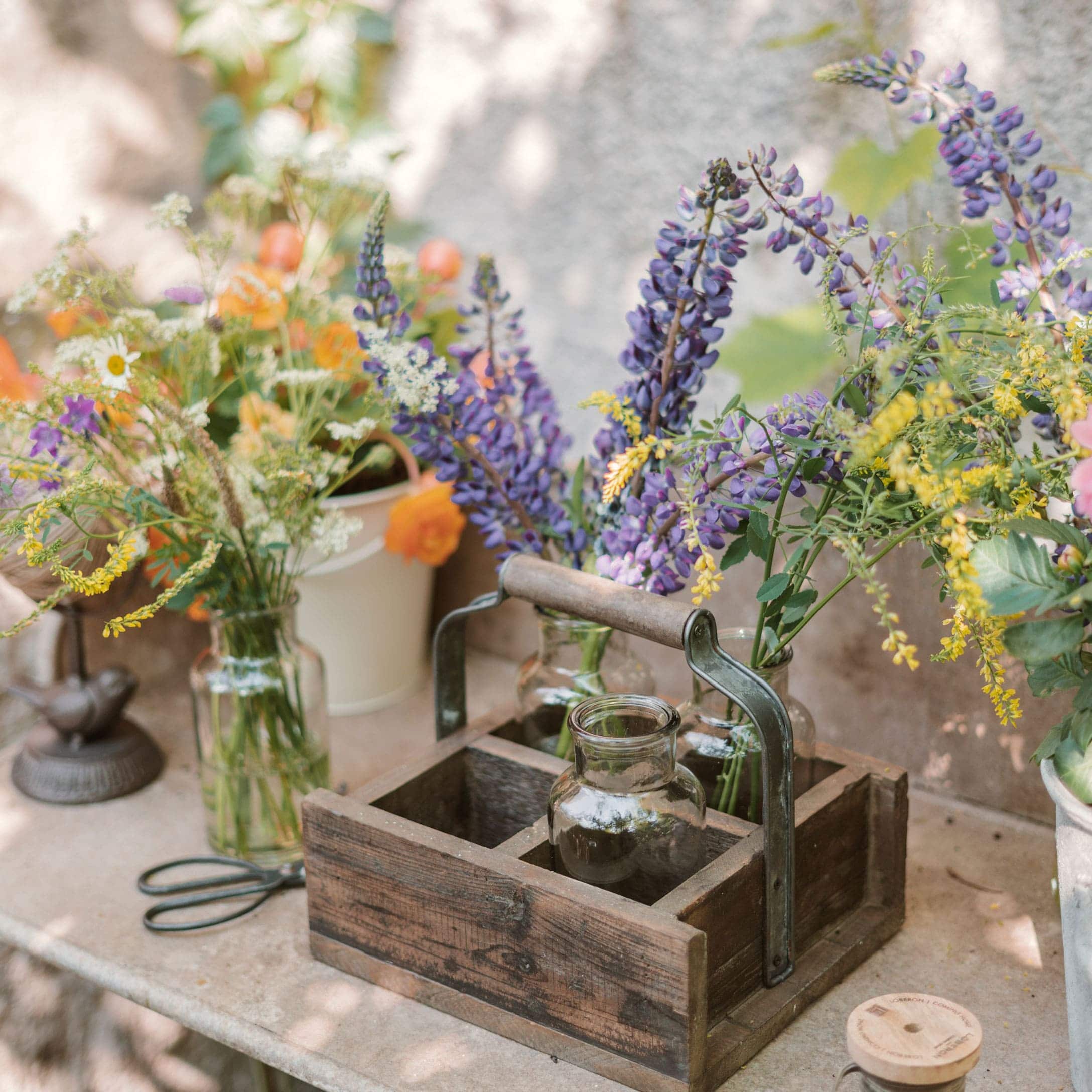 Organizer in legno con manico e vasi di vetro con fiori colorati su tavolo da giardino