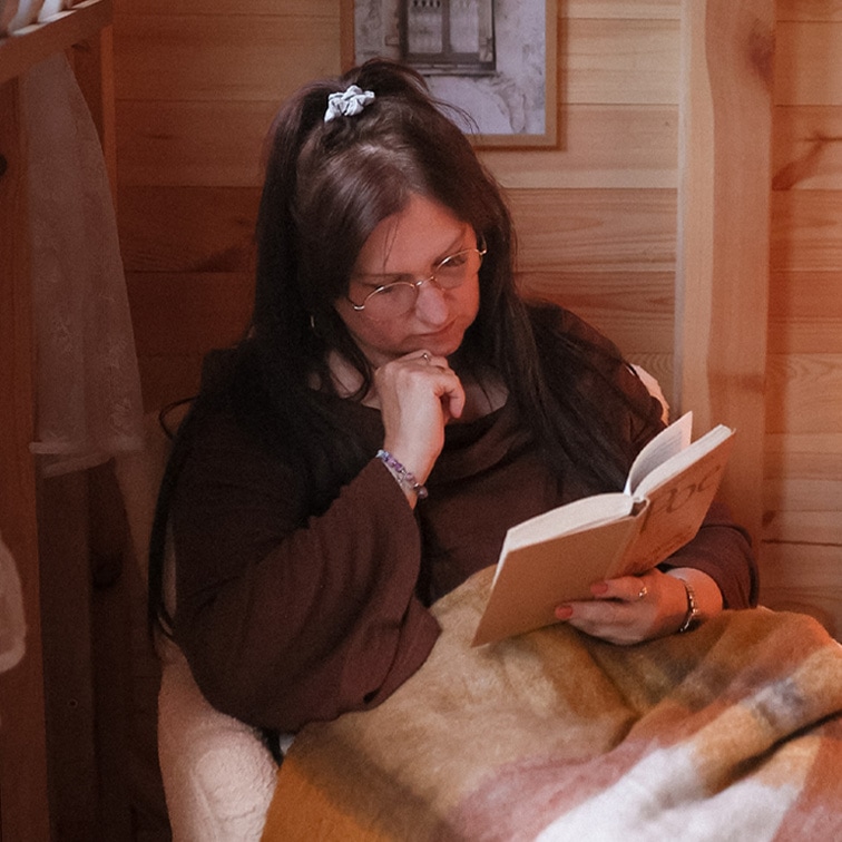 Donna che legge un libro sotto una coperta morbida multicolore in un interno in legno, momento di relax