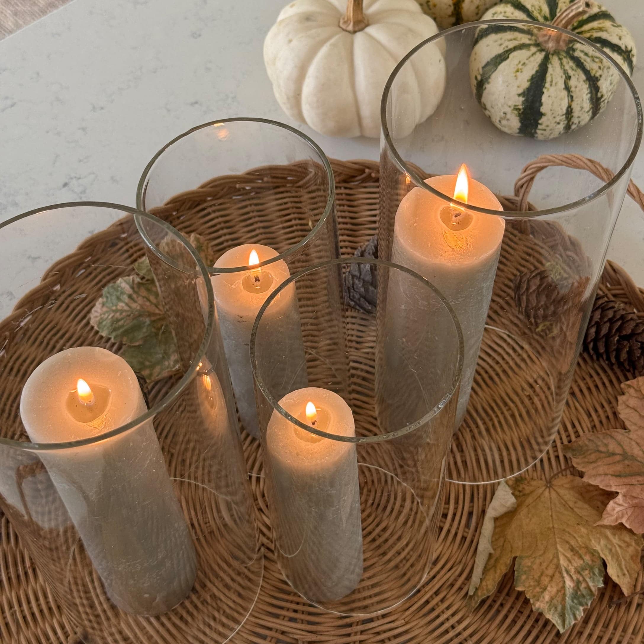 Set di quattro candele bianche in portacandele di vetro su vassoio di vimini con decorazioni autunnali