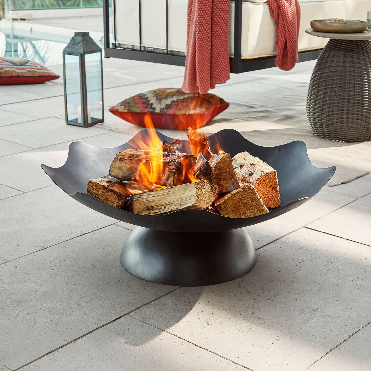 Braciere Ironwell Braciere in metallo nero con legna accesa su terrazza, ideale per giardino e relax all'aperto