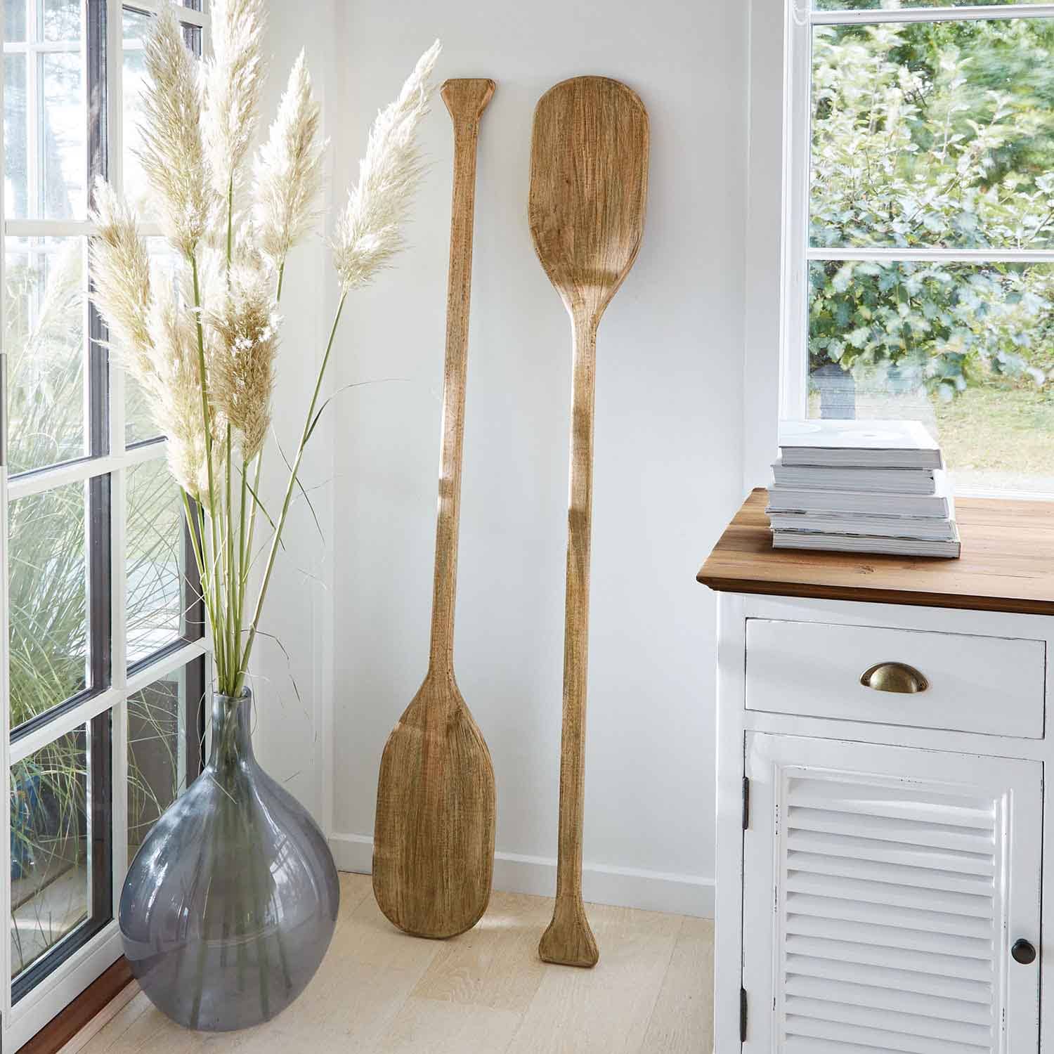 Due pagaie decorative in legno colore naturale appoggiate a parete bianca in interno luminoso
