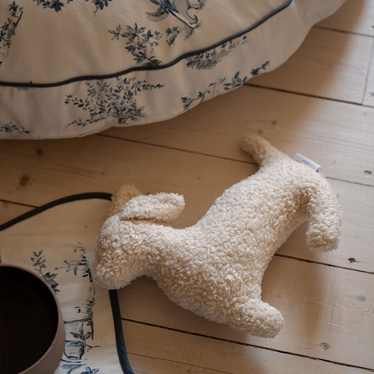 Giocattolo di peluche morbido a forma di cane color crema su pavimento in legno chiaro