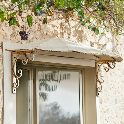 Tettoia in metallo con supporti decorativi invecchiati sopra una finestra su muro in pietra
