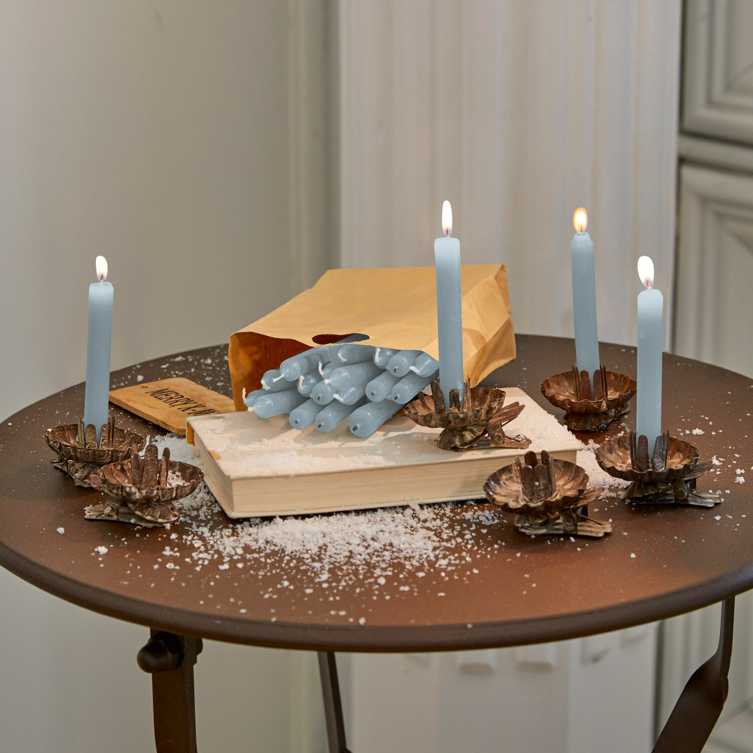 Set di 20 candele Noufa Candele blu con portacandele in ottone su tavolo marrone con libro e busta di carta