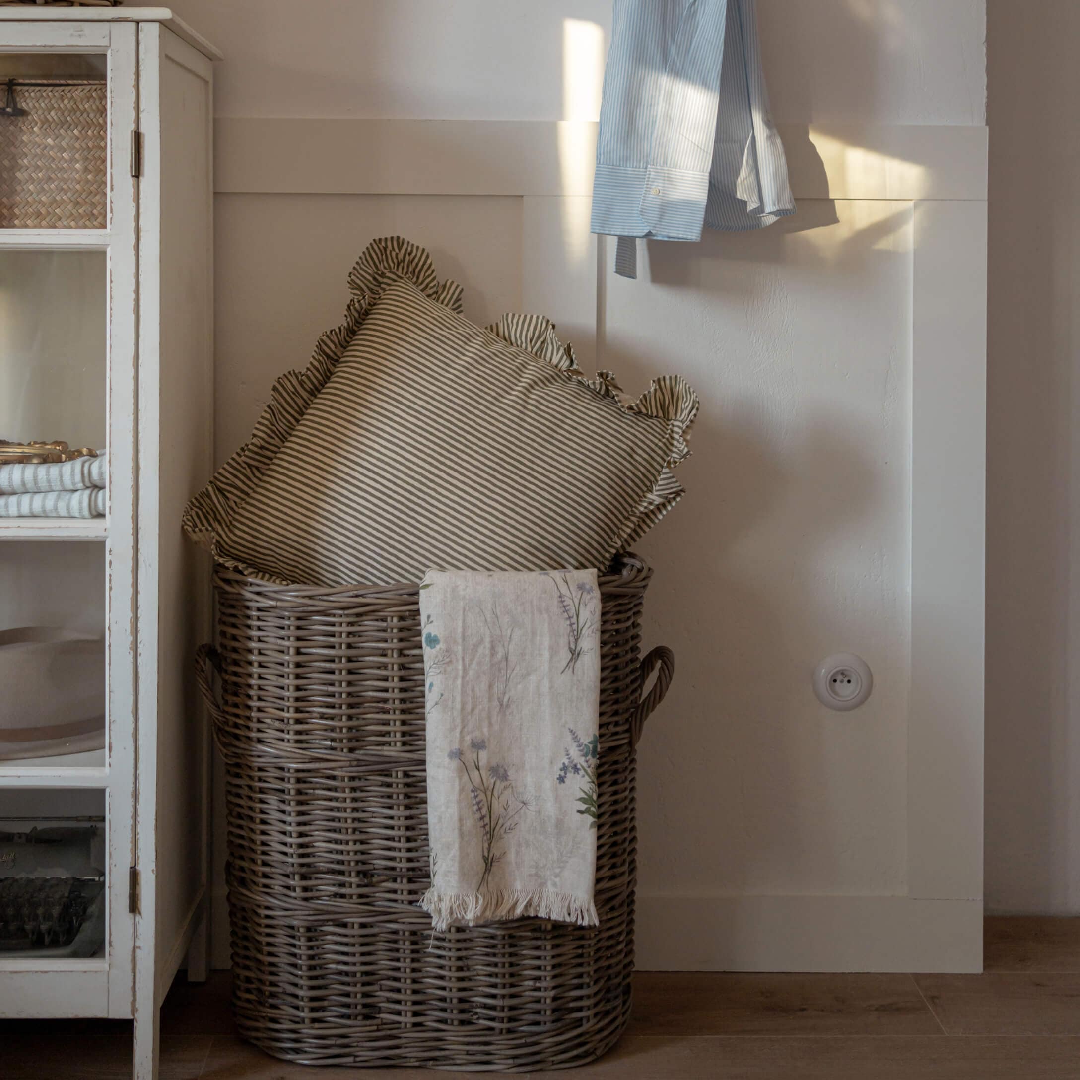 Cesto in vimini marrone con cuscino a righe e coperta di lino con motivo floreale in ambiente accogliente