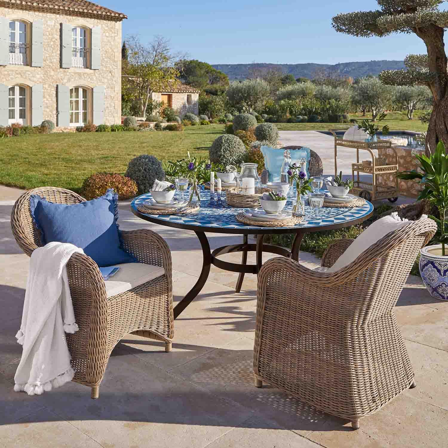 Tavolo rotondo con mosaico blu e sedie in rattan beige su terrazza soleggiata in giardino
