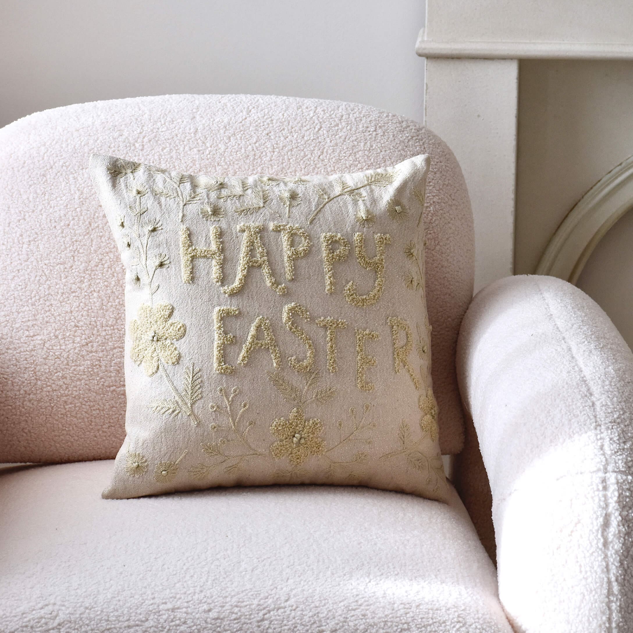 Cuscino decorativo beige con ricamo Happy Easter su poltrona chiara in tonalità pastello
