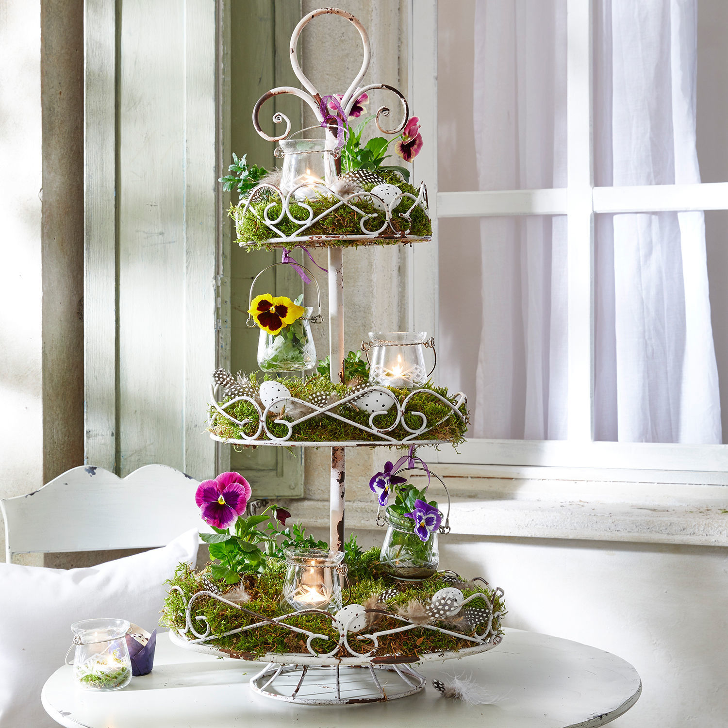 Alzata Julye Porta dolci a tre piani in metallo bianco con muschio, fiori e candele decorativi su tavolo bianco