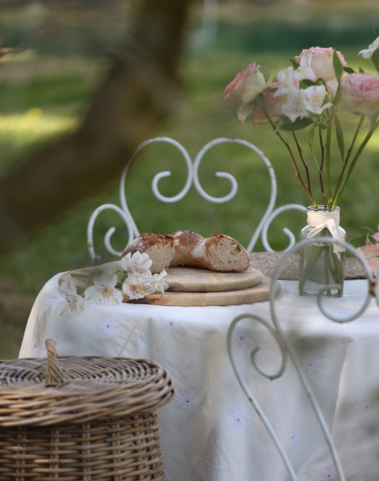 Pane rustico su tagliere di legno su tovaglia bianca con fiori in vaso di vetro in giardino
