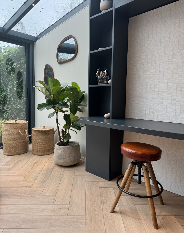 Interno moderno con scrivania nera, sgabello in pelle marrone e vaso in cemento con pianta verde