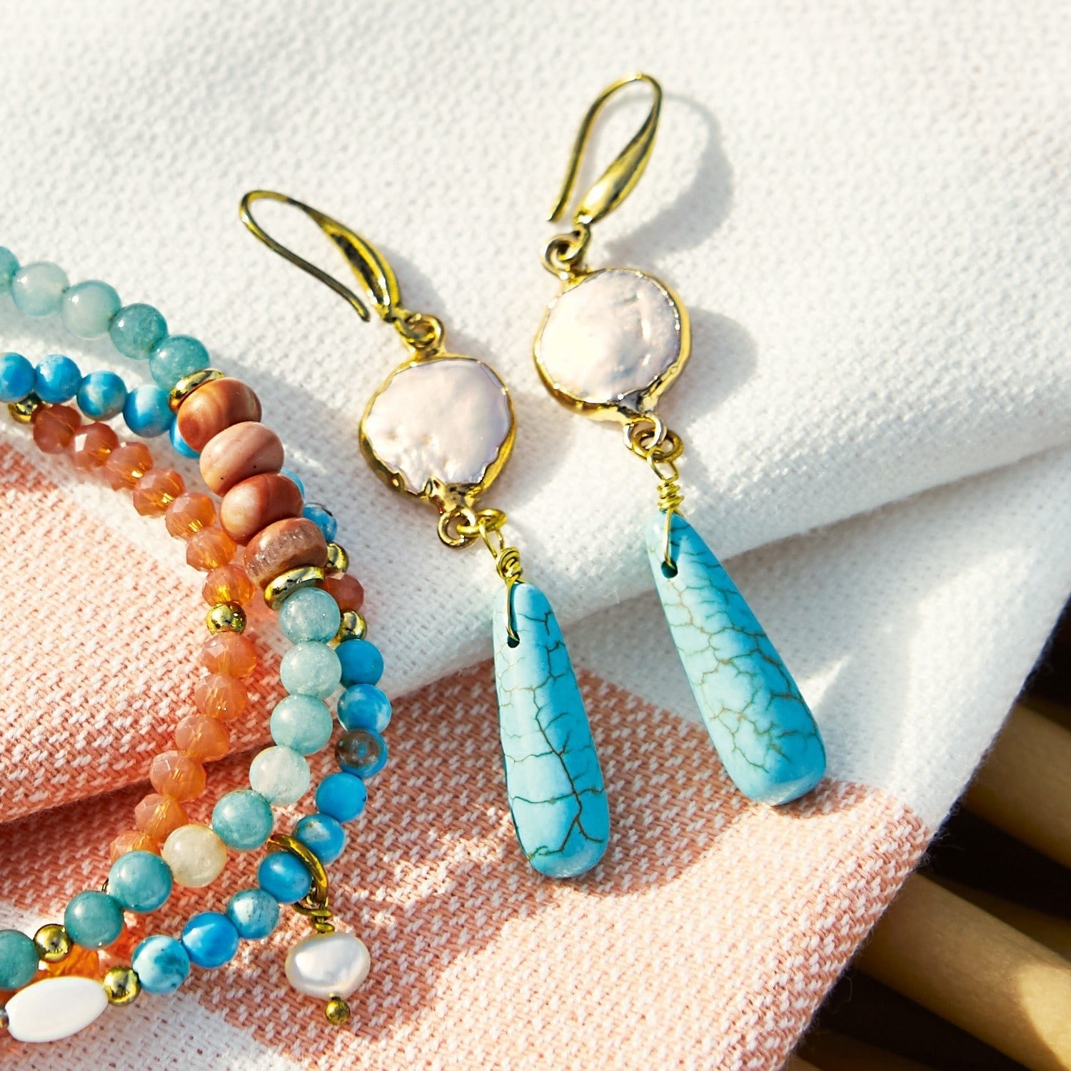 Orecchini Laéna Orecchini con turchese blu e perla bianca su ganci dorati, accanto a braccialetti colorati in pietre naturali
