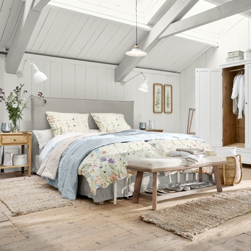 Camera accogliente con letto imbottito grigio chiaro, biancheria da letto floreale, legno naturale e tappeti