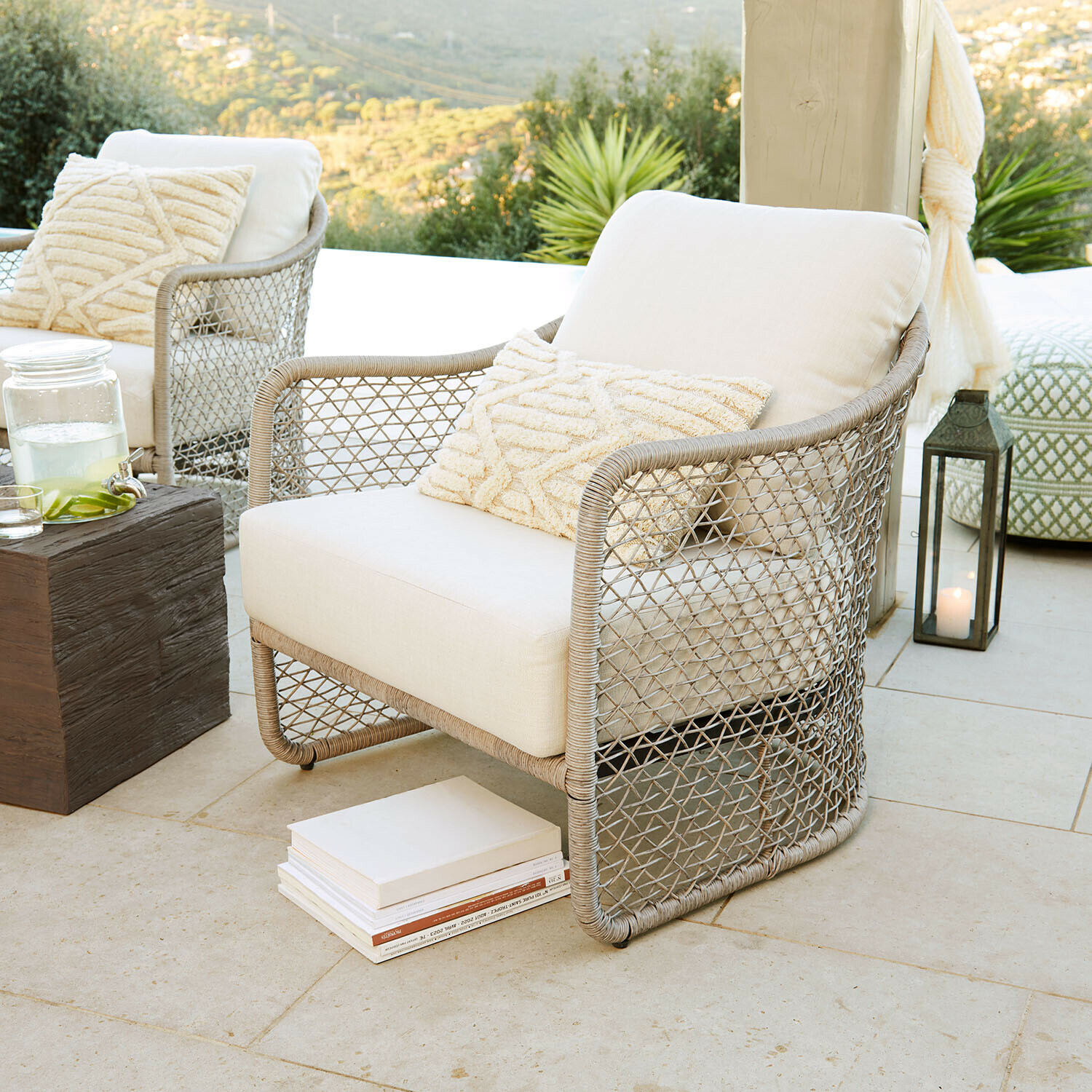 Poltrona da giardino in rattan beige con cuscino crema su terrazza con vista sul verde