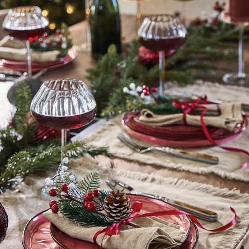 Tavola festiva con piatti rossi, decorazioni naturali e eleganti calici da vino