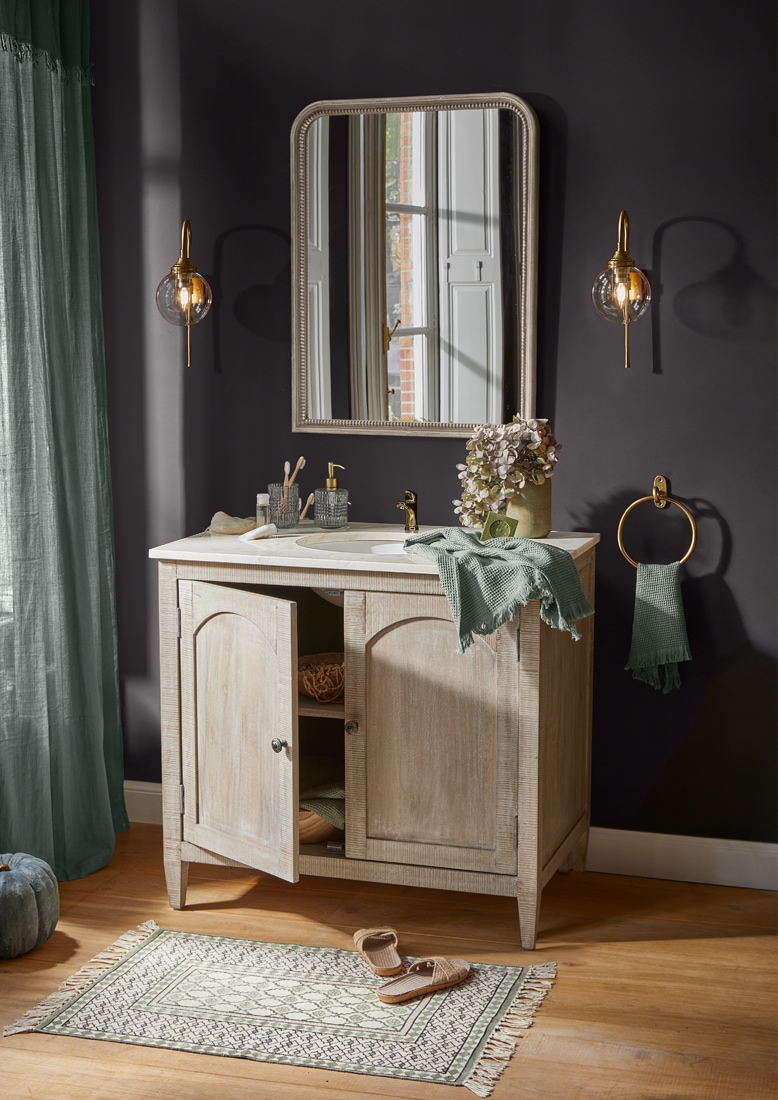 Mobile bagno in legno chiaro con specchio, accessori dorati e asciugamano verde, stile vintage