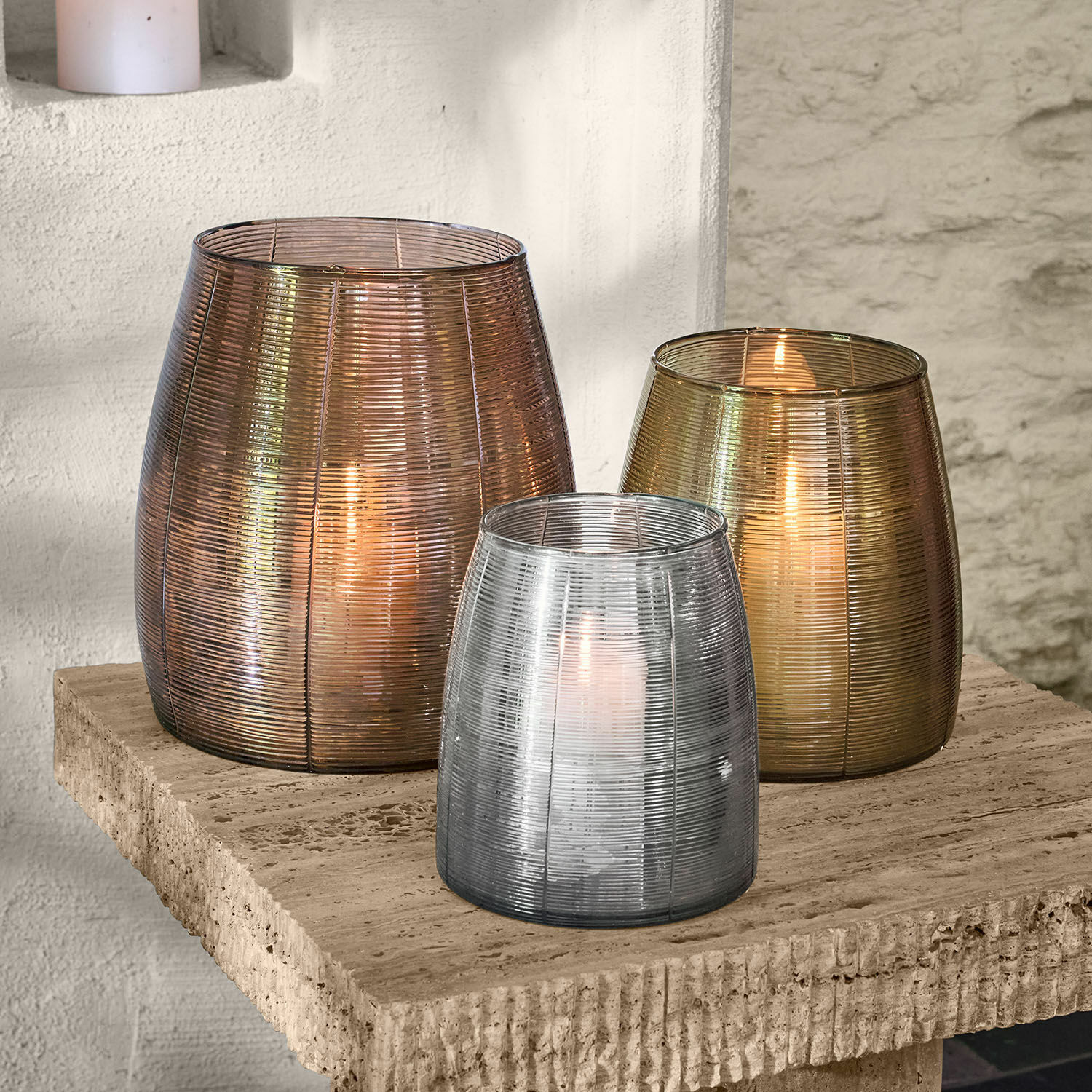 Set di 3 portalumini Uvenar Set di tre lanterne in vetro nei colori bronzo, oro e argento su un piano in pietra