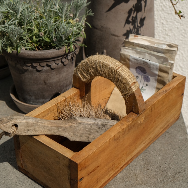 Scatola di legno con manico avvolto in corda, contiene spazzola e bustine di semi, materiali naturali