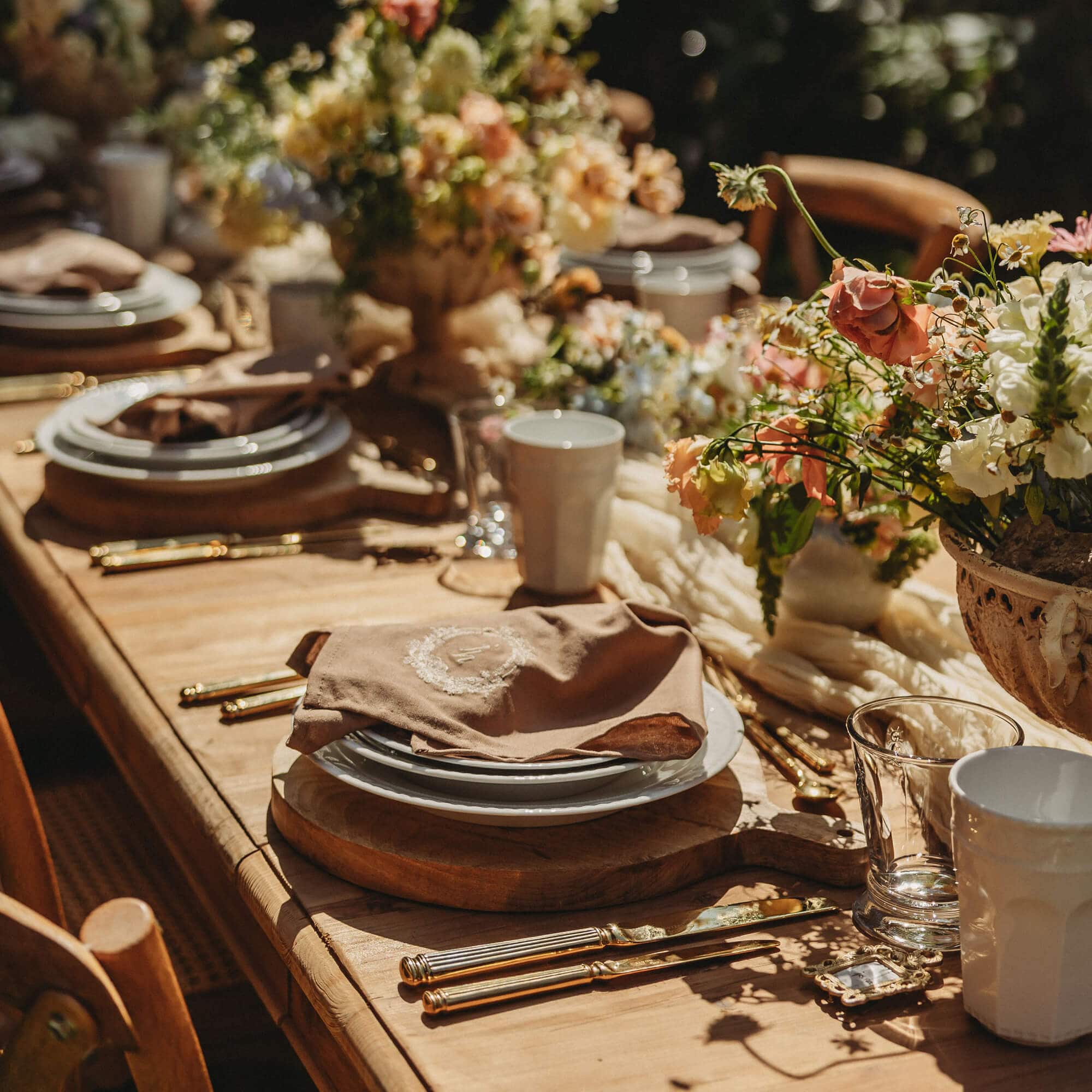 Tavolo rustico in legno con stoviglie, posate dorate e decorazioni floreali per evento elegante