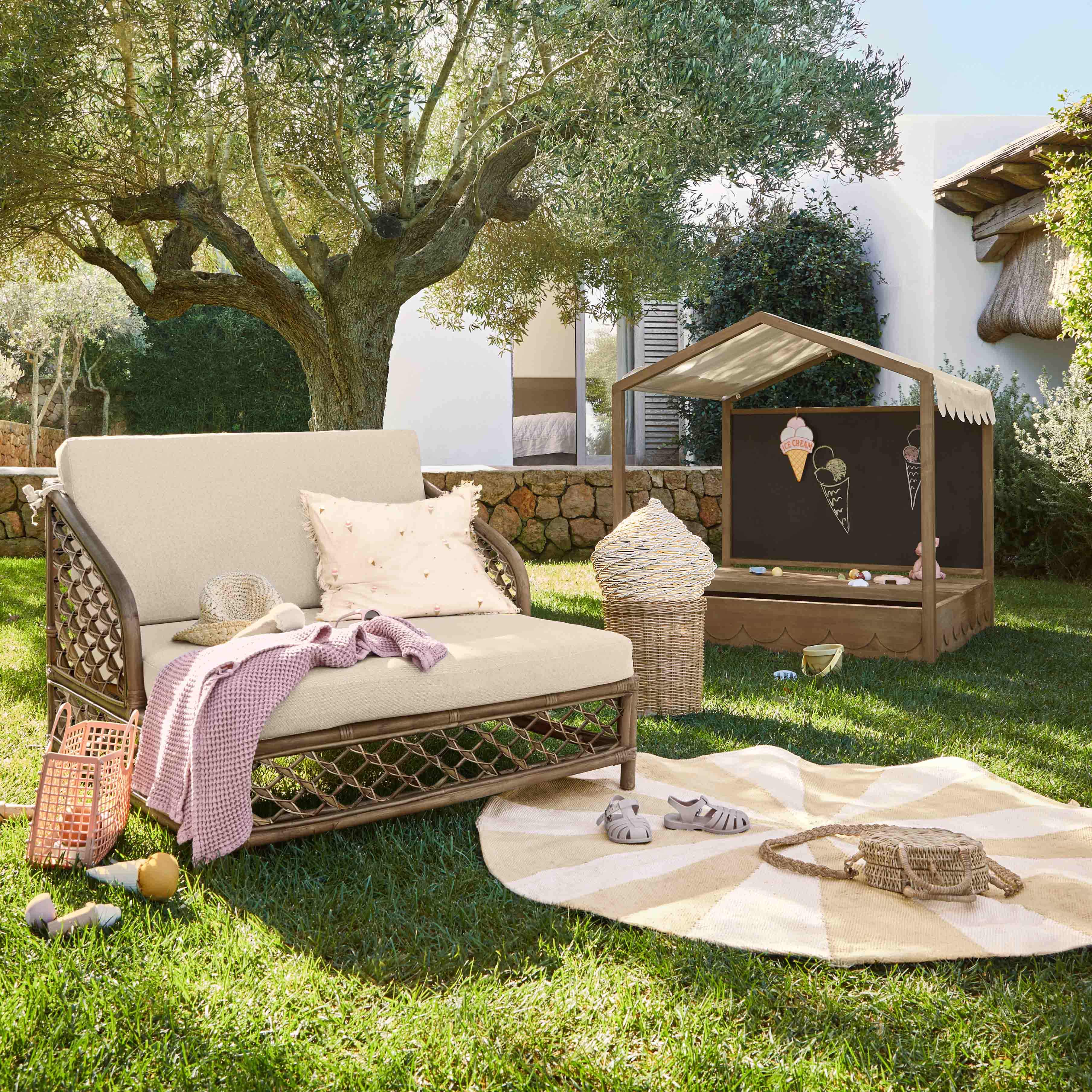 Giardino con sdraio beige, cuscino e coperta rosa sull'erba sotto un ulivo