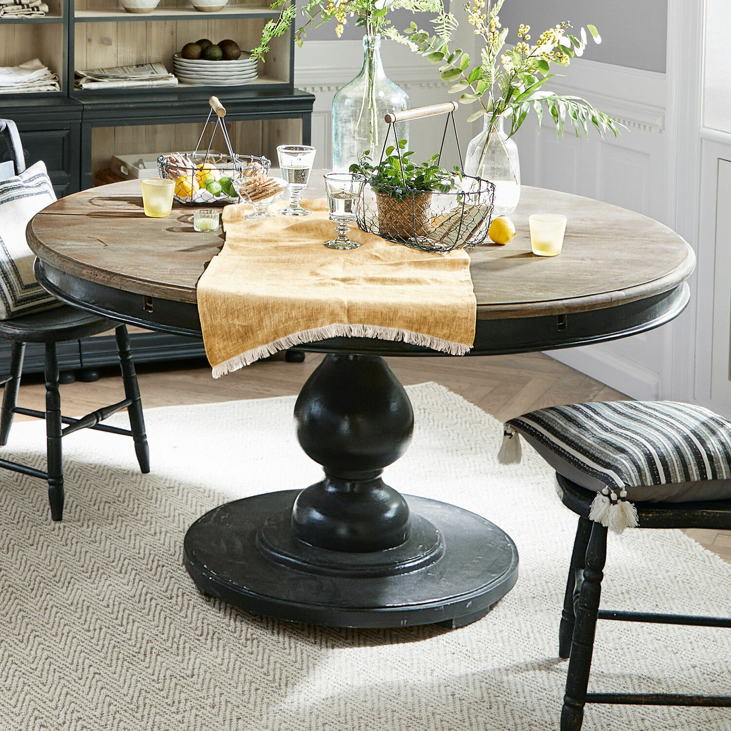 Tavolo Shrewsbury Tavolo rotondo in legno con base nera e decorazioni su tovaglia beige in sala da pranzo