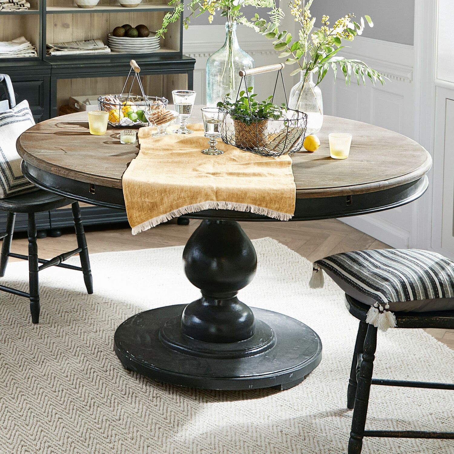 Tavolo Shrewsbury Tavolo rotondo in legno con base nera e decorazioni su tovaglia beige in sala da pranzo