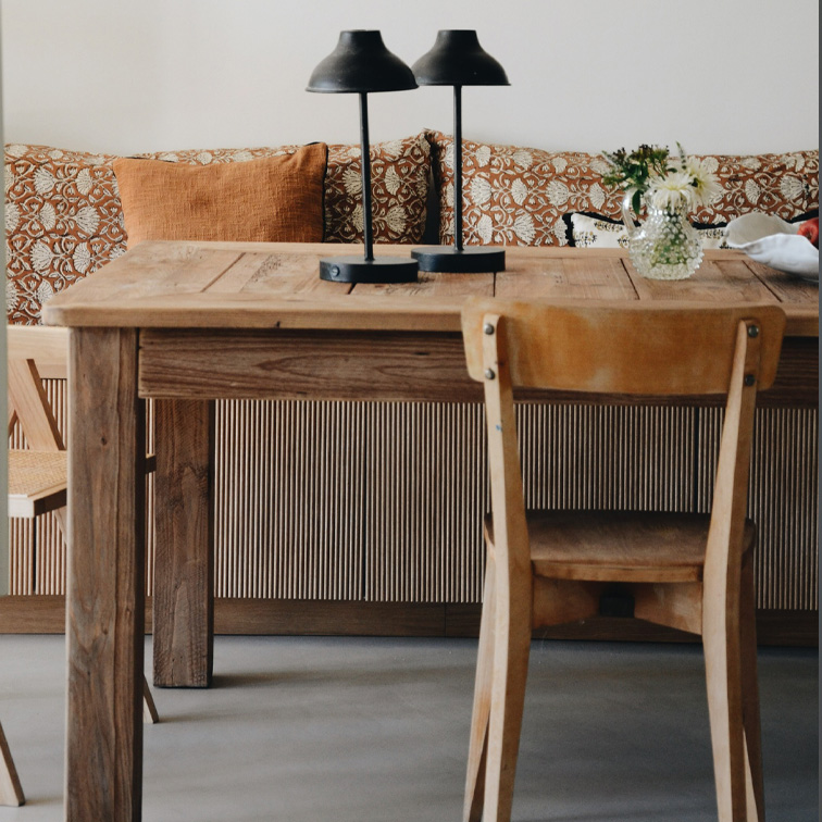 Tavolo in legno con due lampade nere e fiori in vaso davanti a divano con cuscini arancioni