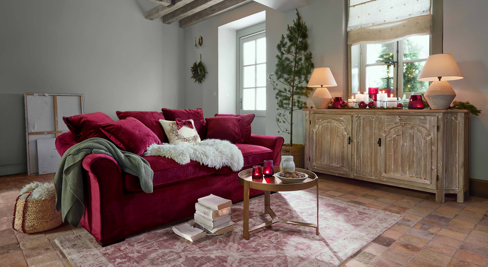 Divano in velluto rosso con cuscini e coperta verde in soggiorno accogliente con credenza in legno e decorazioni natalizie