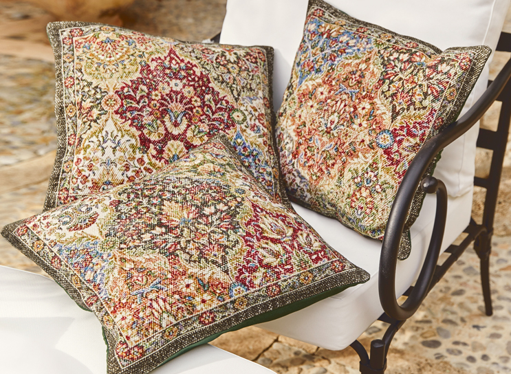 Tre cuscini decorativi con motivo orientale in colori caldi su sedia bianca in metallo