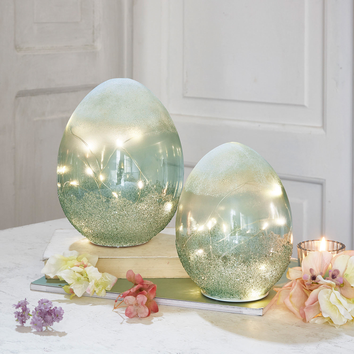 Coppia di uova con luci a LED Borleos Uova decorative in vetro verde con luci LED integrate su tavolo con fiori e candela
