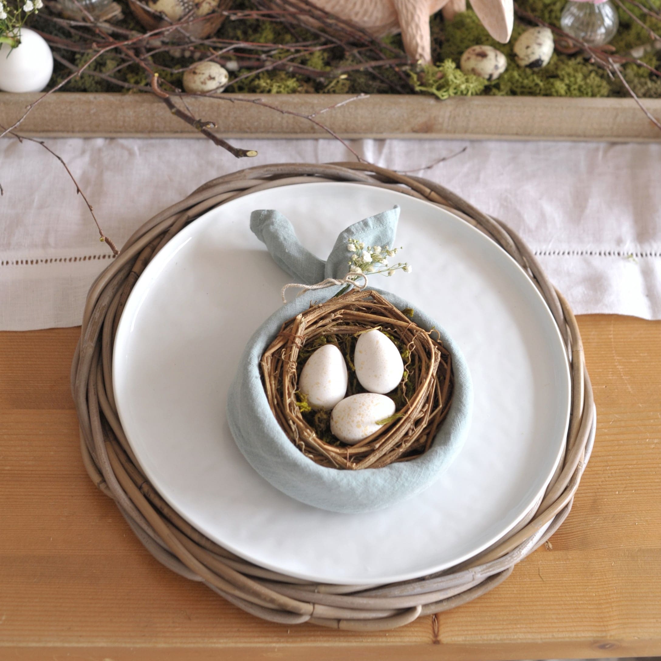 Decorazione da tavola con piatto bianco, sottopiatto in vimini e tovagliolo con nido e uova
