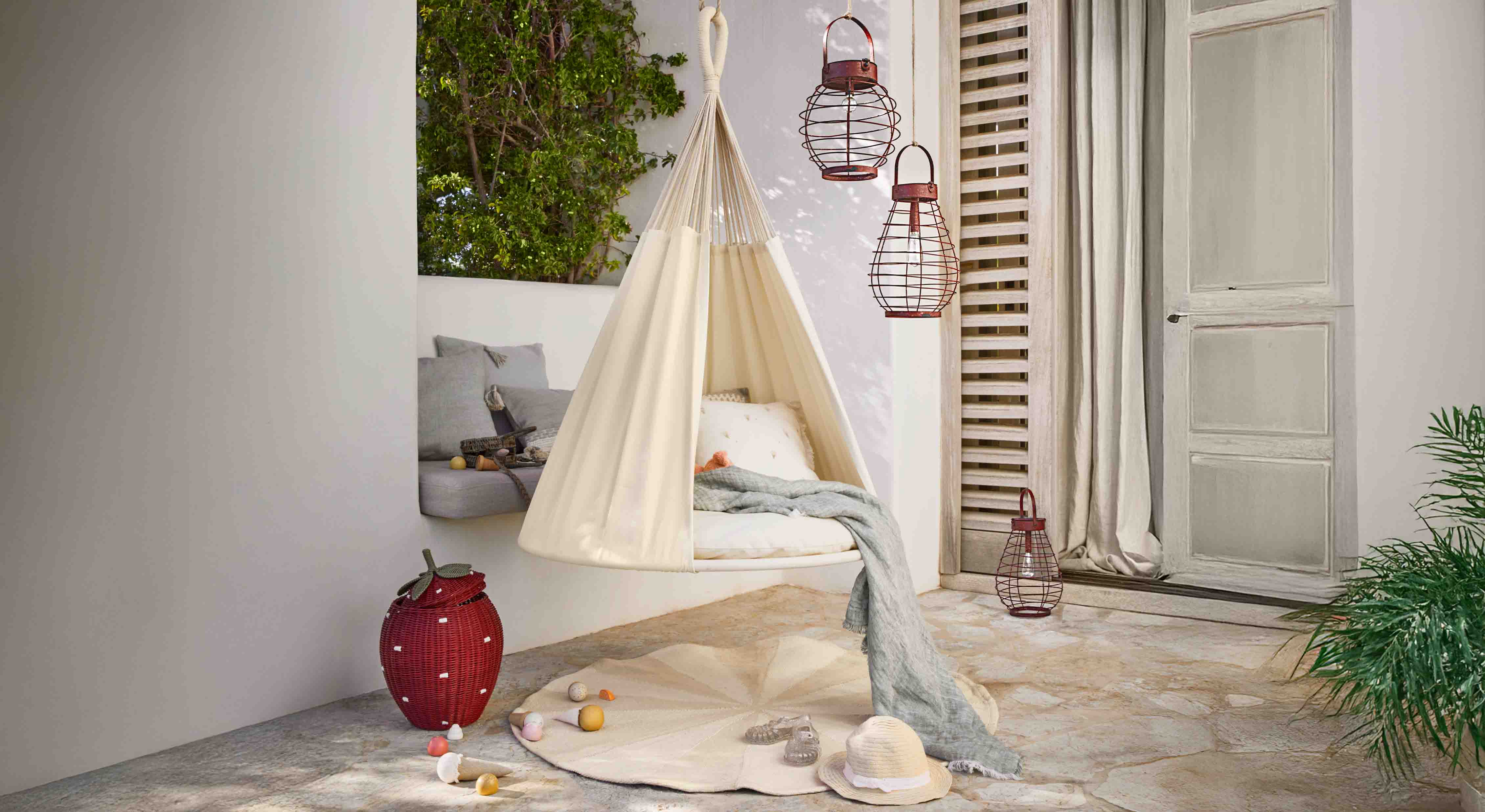 Poltrona sospesa beige in tessuto su terrazza con cuscini e lanterne decorative in metallo
