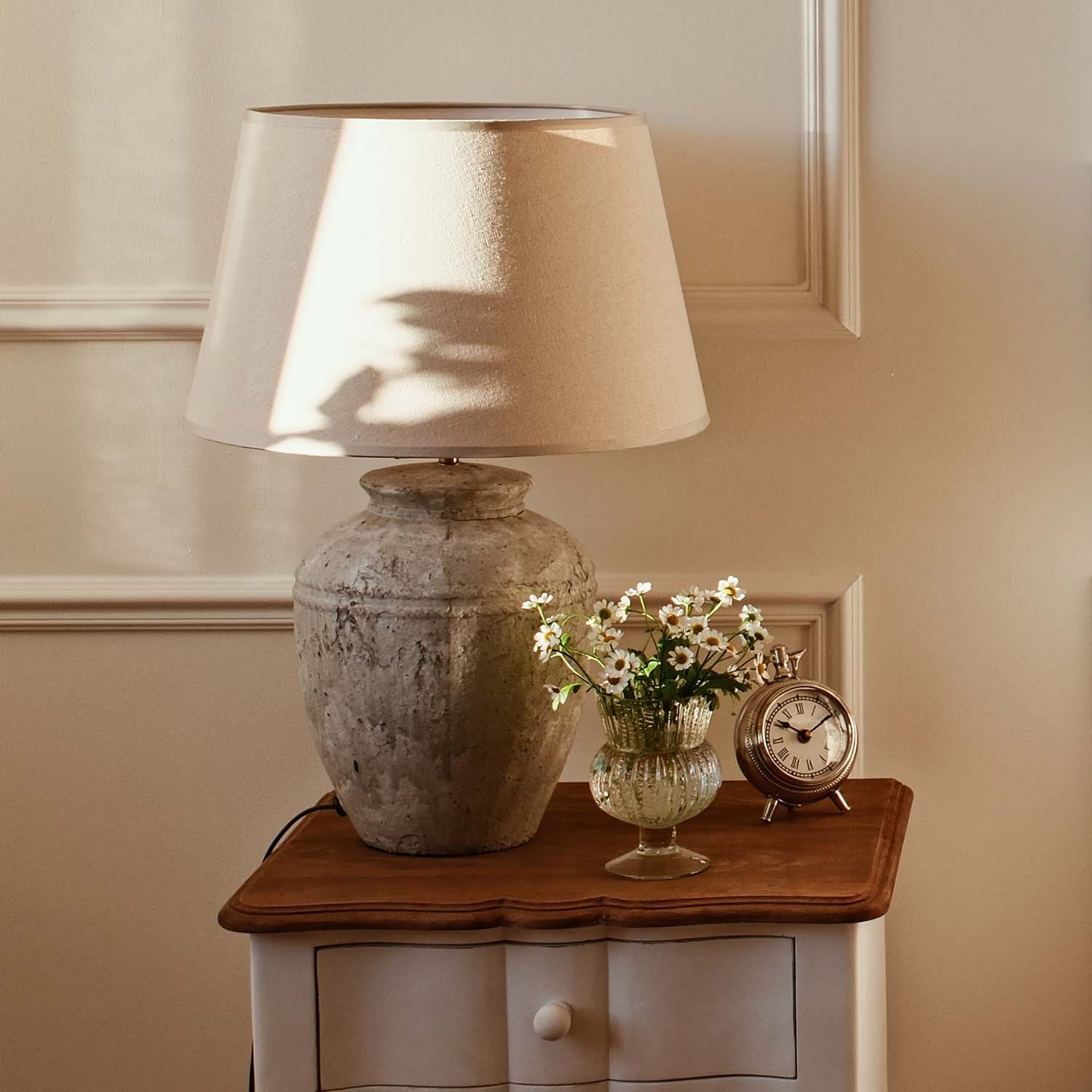 Lampada da tavolo con paralume beige e base in ceramica vintage su tavolo in legno con fiori e orologio