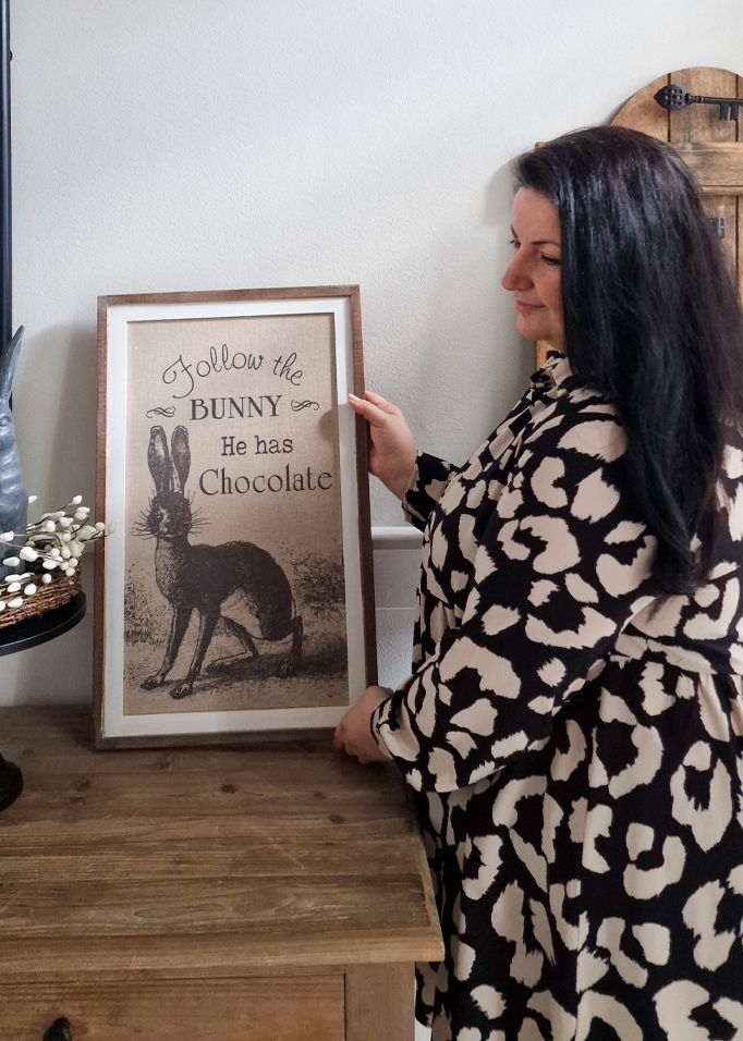 Donna che tiene una cornice con immagine di coniglio e testo sul cioccolato su tavolo in legno