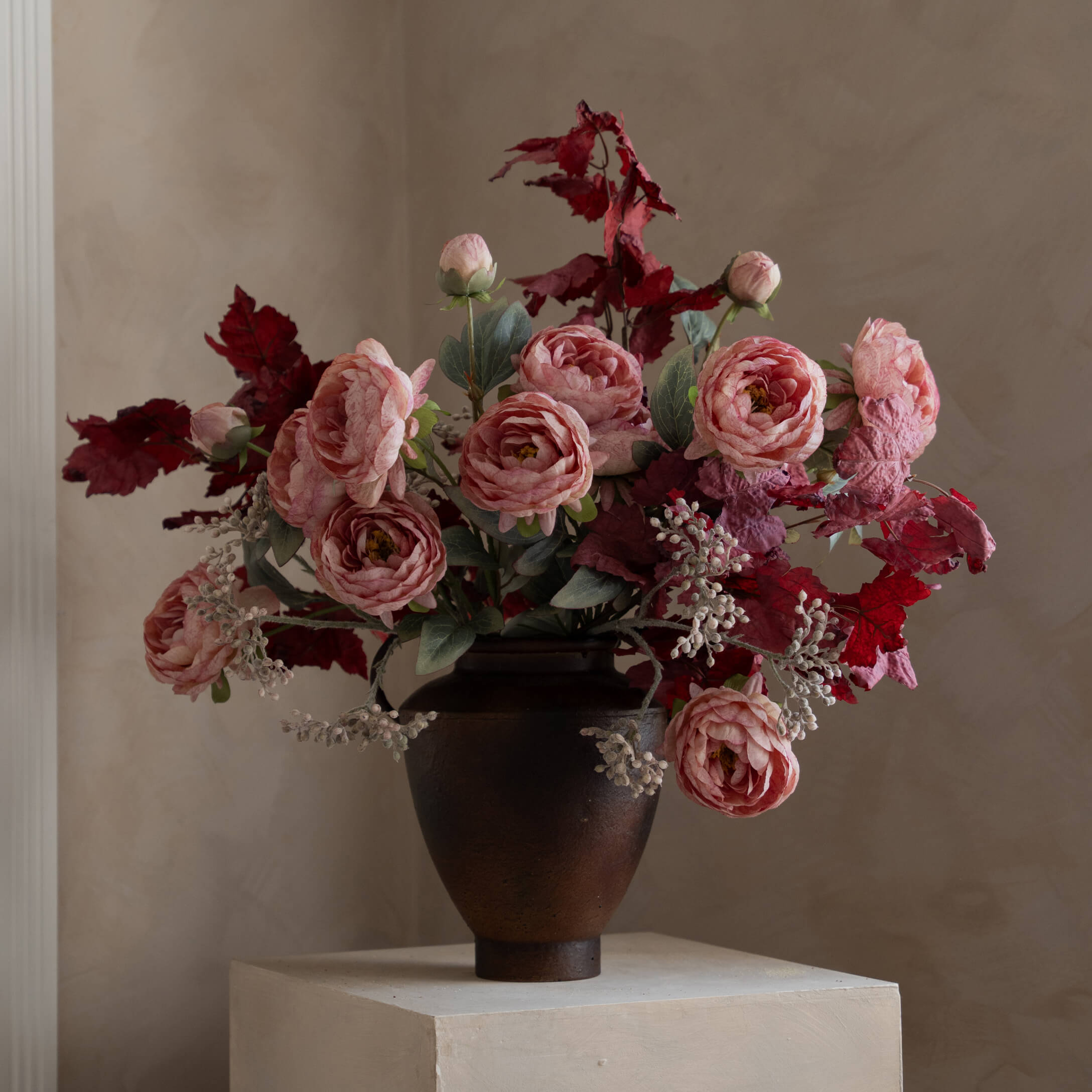 Mazetto di rose rosa e foglie rosse in vaso di ceramica scura su piedistallo chiaro