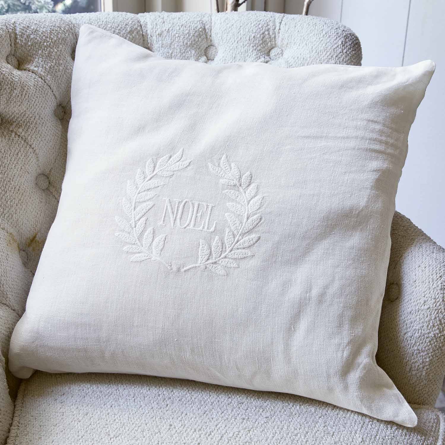 Cuscino bianco in lino con ricamo NOEL e corona decorativa su poltrona chiara, accessorio natalizio