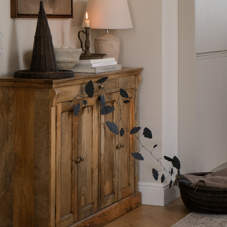 Credenza in legno con ghirlanda di foglie nere e lampada da tavolo in ambiente accogliente