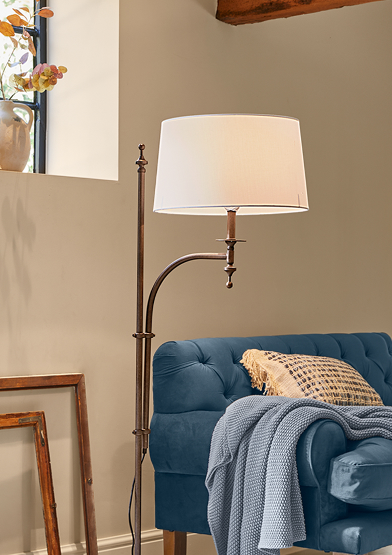 Lampada da terra in metallo con paralume bianco accanto a divano blu con coperta lavorata a maglia