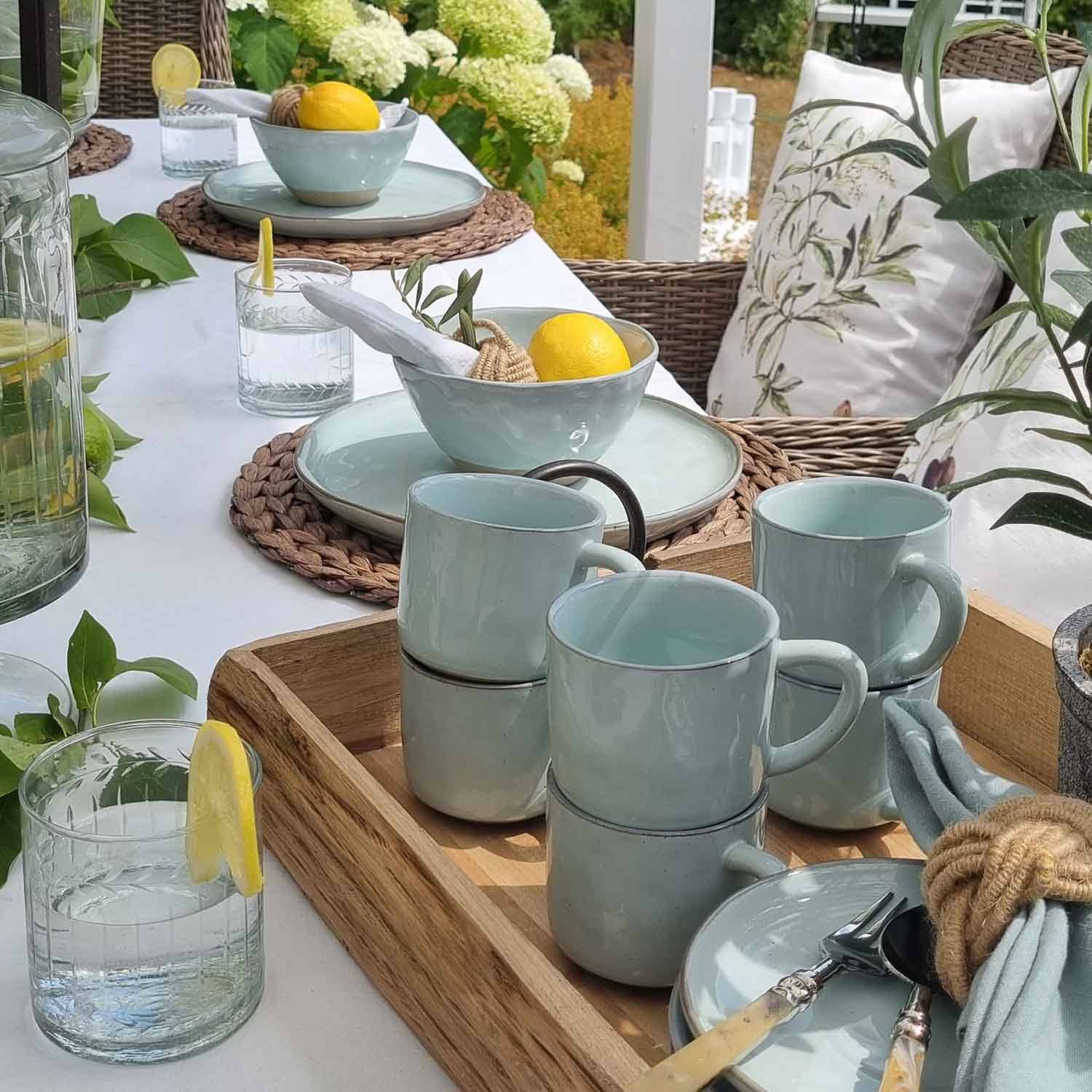 Set di stoviglie in ceramica azzurro chiaro su vassoio in legno con limoni e bicchieri d'acqua