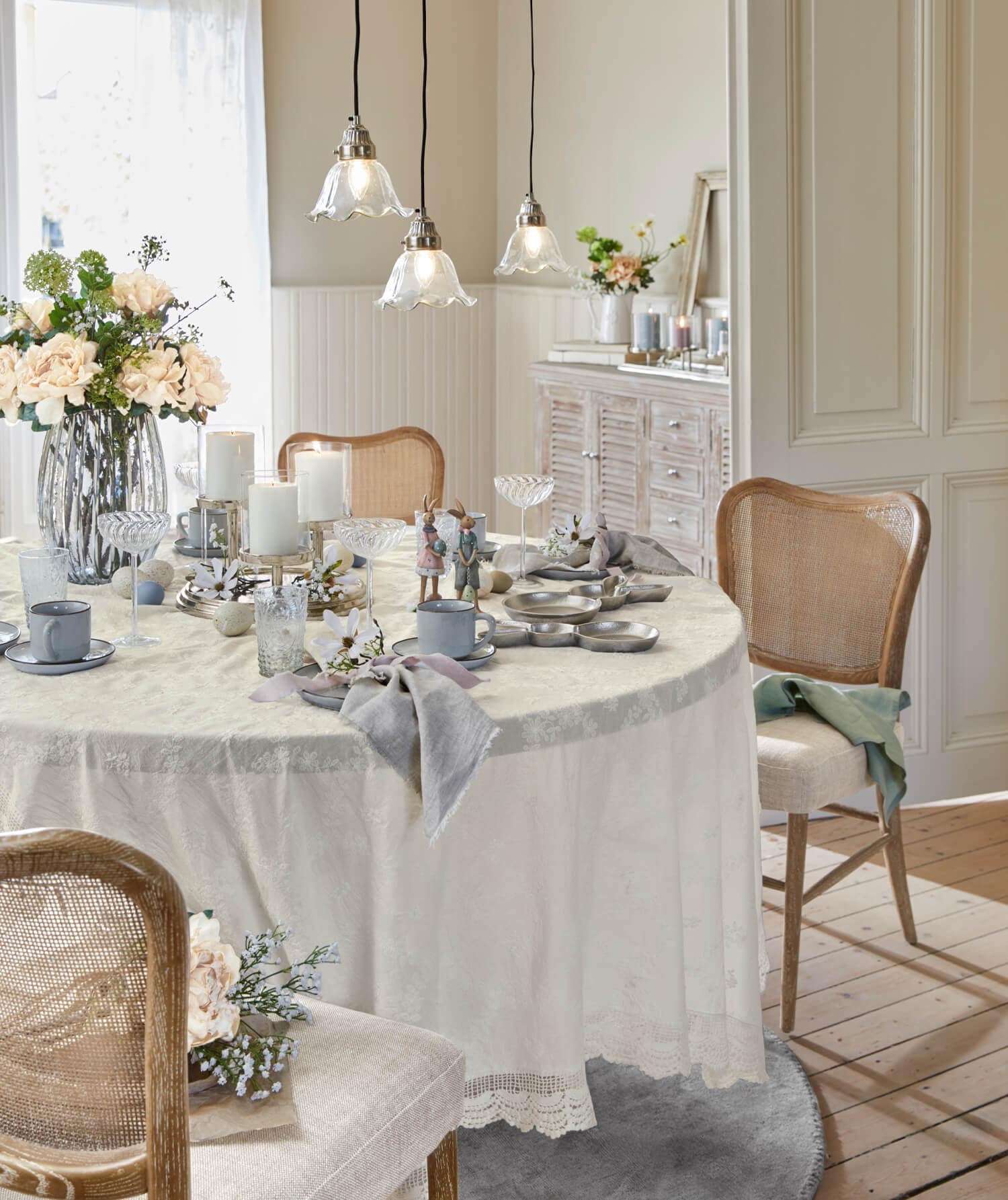 Tavolo chiaro con tovaglia crema e decorazioni rustiche, sedie in legno e fiori in sala da pranzo luminosa